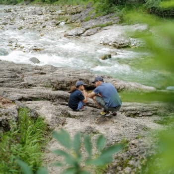 Papa und Kind sitzen am Fluss im Familienurlaub in Tirol